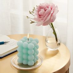 a pink rose sitting on top of a table next to a candle