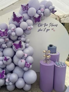 there is a purple and white balloon arch with butterfly decorations on it, along with other balloons