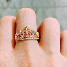 a woman's hand holding a gold ring with an orange and white diamond crown on it