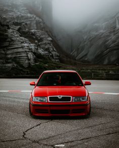 a red car is driving down the road in front of some mountains and foggy skies