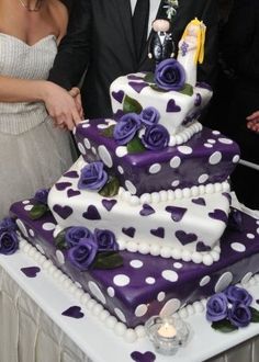 a man and woman cutting into a wedding cake with purple roses on it at a reception