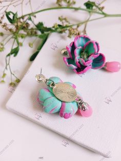 two pink and blue flowers sitting on top of a piece of paper next to each other