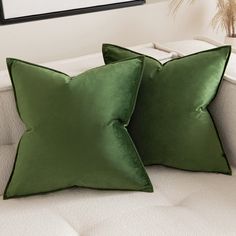 two green pillows sitting on top of a white couch in front of a framed photograph