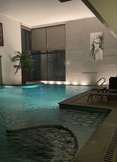 an indoor swimming pool with blue water and lights on the walls, in front of a large window