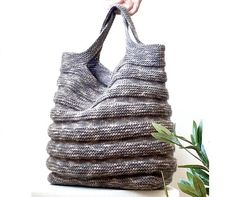 a hand holding a gray knitted bag on top of a white table next to a plant