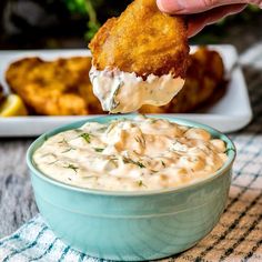 a person dipping some kind of food into a blue bowl with white sauce on it