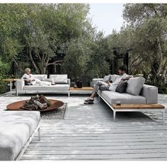 two people sitting on couches in the middle of a wooden deck with trees and bushes