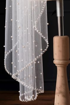 a white veil with pearls hanging from it's side on a wooden pole next to a window