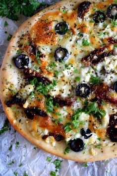 a pizza with olives, cheese and parsley on it sitting on wax paper