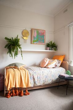 a bedroom with a bed, plant and pictures on the wall above it's headboard