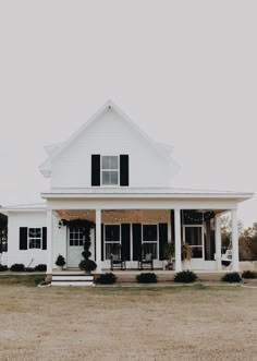 a large white house with black shutters on the front and side windows, sitting in an open field