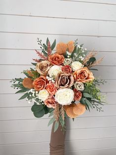 a bridal bouquet with orange and white flowers in front of a wooden wall background