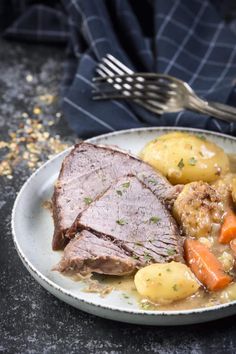 a plate with meat, potatoes and carrots on it next to a silver fork