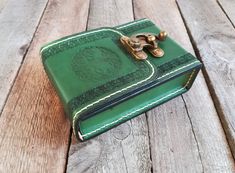 a green leather book with a golden handle on a wooden surface, sitting on top of a table