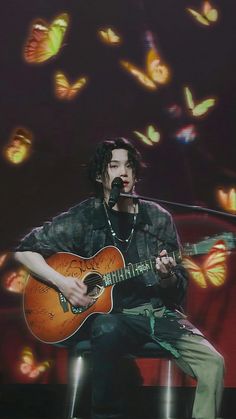 a man sitting in front of a microphone while holding a guitar