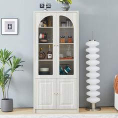 a tall white cabinet with glass doors and shelves in the corner next to a potted plant