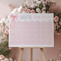 a calendar with pink ribbon on it sitting next to flowers and greenery in front of a pink wall