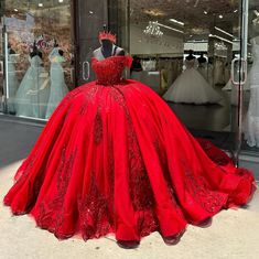 a red ball gown on display in front of a store window with mannequins