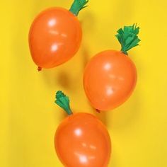 three orange carrots with green tops on a yellow background, one is larger than the other