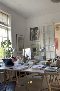 an office with lots of clutter on the desk and in front of two windows