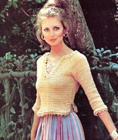 a woman wearing a yellow top and purple skirt with her hands on her hips, standing in front of a tree