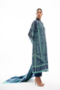 A printed navy blue cotton net shirt is adorned with elegant lacework in a turquoise hue and scalloped edging. Featuring worked buttons on the neckline, the shirt is paired with a matching printed dupatta and rawsilk trousers. Blue Sets With Printed Motifs In Straight Kurta Style, Blue Bollywood Lawn Suit With Printed Motifs, Bollywood Blue Lawn Suit With Printed Motifs, Blue Chanderi Lawn Suit With Printed Motifs, Blue Unstitched Dupatta With Printed Motifs, Blue Chikankari Embroidered Palazzo Set In Cambric, Blue Saree Sets With Printed Motifs, Bohemian Blue Lawn Suit For Festive Occasions, Blue Cambric Palazzo Set For Eid