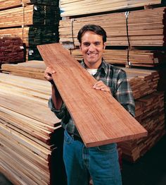 a man holding a piece of wood in front of stacks of wooden planks at a lumber store