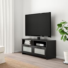 a flat screen tv sitting on top of a black entertainment center next to a plant