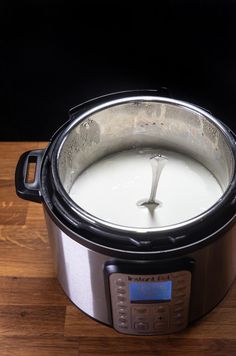 a slow cooker filled with milk on top of a wooden table