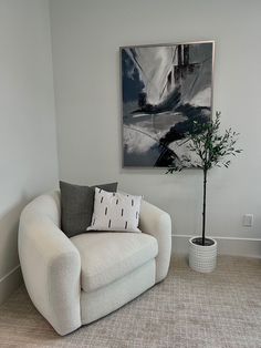 a white chair sitting next to a potted plant in front of a painting on the wall