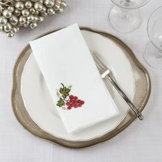 a white plate topped with a napkin next to wine glasses and silver balls on top of a table