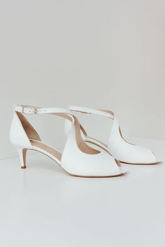 two white high heels with straps on each side and one heeled shoe in the middle