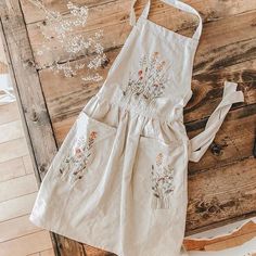 a white apron with flowers on it sitting on a wooden table