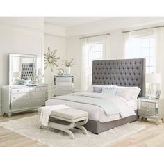 a bedroom with white walls and wooden flooring has a gray upholstered bed