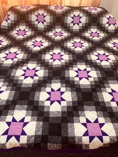 a bed with a purple and black quilt on it's cover, next to a window