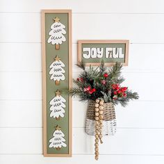 a christmas decoration with pine cones and berries hanging on the wall next to a sign that says joyful