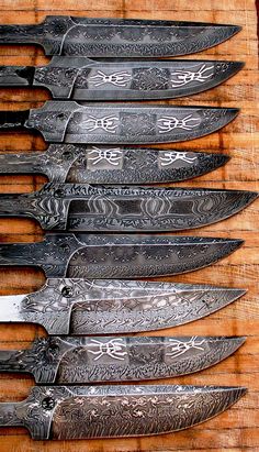 five knives are lined up on a wooden surface with intricate designs and patterns around them