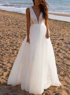 a woman standing on top of a sandy beach next to the ocean wearing a white dress