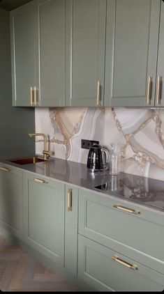 a kitchen with green cabinets and marble counter tops, gold handles on the faucet