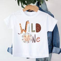 Wild One Safari Animals T-shirt T-shirt is 100% cotton.  We design & print our products with care & love! We use the best quality vinyls, inks & transfers on all products. * * * * * * * * * * * * * * * * * * * * * * * * * * * * * CARE INSTRUCTIONS: Wash inside out on gentle wash, Do not tumble dry. * * * * * * * * * * * * * * * * * * * * * * * * * * * * * SHIPPING: We want to get your product to you as quickly as possible, your purchase will be shipped through Australia post, Express post is available for selection. * * * * * * * * * * * * * * * * * * * * * * * * * * * * * GUARANTEE: We stand behind our products with a 100% guarantee; if you are unsatisfied with our product, please let us know & we will rectify any issues. We are unable to refund products due to change of mind or those tha First Birthday Funny Print Crew Neck T-shirt, First Birthday Graphic Tee With Name Print, Cotton Graphic Print T-shirt For Birthday, Graphic Tee With Name Print For First Birthday, Casual T-shirt With Funny Print For First Birthday, First Birthday Graphic Tee With Short Sleeves, Fun Graphic Print T-shirt For First Birthday, Character Print Cotton T-shirt For Birthdays, Casual Crew Neck T-shirt For First Birthday