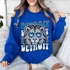 a woman sitting on a bed wearing a blue sweatshirt with the words detroit printed on it