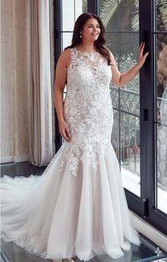 a woman standing in front of a window wearing a wedding dress