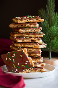 a stack of chocolate and sprinkle covered cookies on a plate next to a christmas tree