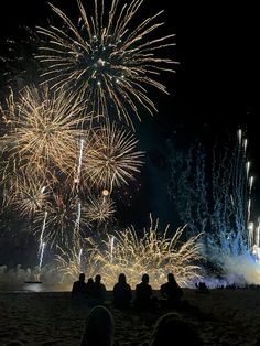 people are sitting on the beach watching fireworks