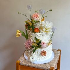 a white cake with flowers on top sitting on a wooden chair next to a wall