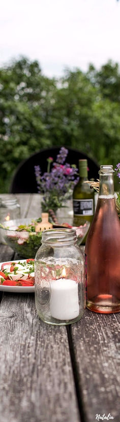 an outdoor table with flowers and jars on it