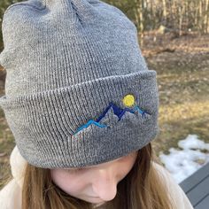 "Keep your head and ears warm this winter with our stylish mountain beanie hat! The cuff features a beautiful embroidered design of mountains and a moon, making it the perfect finishing touch to any winter outfit. Made from 100% acrylic, this hat is sure to keep you cozy all season long. 100% acrylic knit 12\" knit Adjustable cuff, shown as 3\"" Winter Hats For Outdoor Activities, Gray Hats For Winter Outdoor Activities, Gray Hats For Outdoor Winter Activities, Gray Hats For Outdoor Activities In Winter, Winter Outdoor Cap, Winter Hiking Cap, Winter Windproof Beanie For Outdoor Activities, Winter Outdoor Hat With Adjustable Fit, Winter Camping Hat, One Size Fits Most