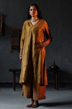 Antique gold flared kurta in a handloom tissue base with embroidery on the sleeve hems. Comes with farshi pants.
Component: 2
Pattern: Embroidery
Neckline: V neck
Sleeve Type: Full
Fabric: Handloom Tissue; Lining: Shantoon
Color: Gold
Other Details: 
Pockets on the sides
Side slits
Note: Dupatta worn by the model is not for sale
Occasion: Puja - Aza Fashions Embroidery Neckline, Gold Suit, Black Lehenga, Traditional Suit, Kurta Patterns, Pakistani Wedding Outfits, A Line Kurta, Traditional Indian Outfits, Kurti Designs Party Wear