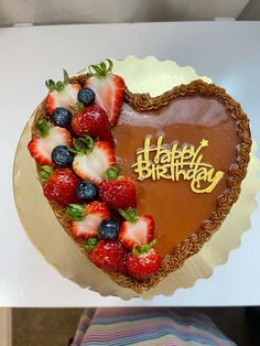 a heart - shaped cake with strawberries and blueberries on the top is decorated with happy birthday