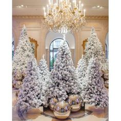 christmas trees in the lobby of a hotel decorated with white and silver decorations, surrounded by chandeliers